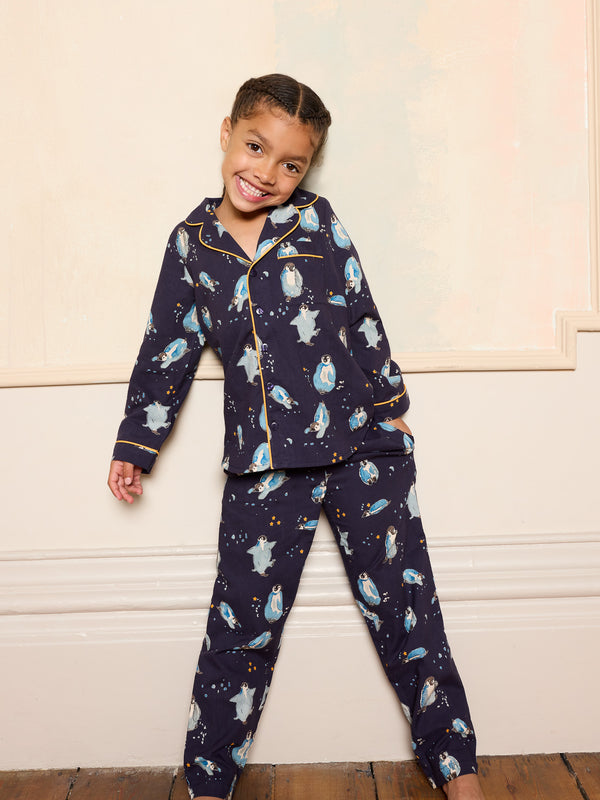 Child wearing a navy blue pyjama set with penguin print smiling against a neutral wall.