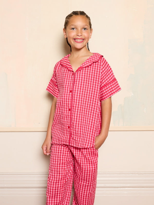 Girl wearing a pink checkered pyjama set against a beige background