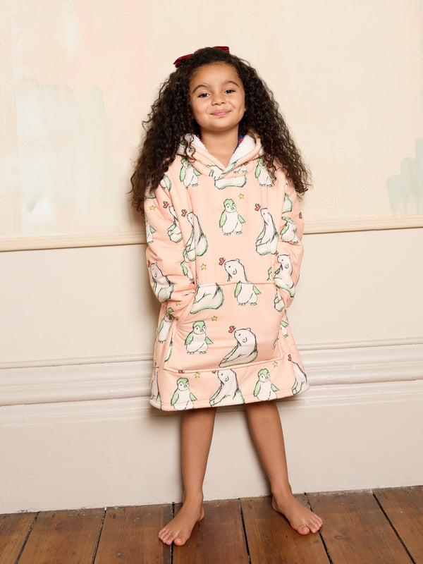 Young girl wearing a pink oversized blanket hoodie with polar bear pattern against a beige wall.