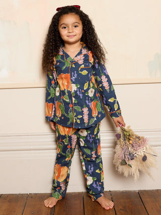 Child wearing a pumpkin pyjama set holding dried flowers against a white wall.