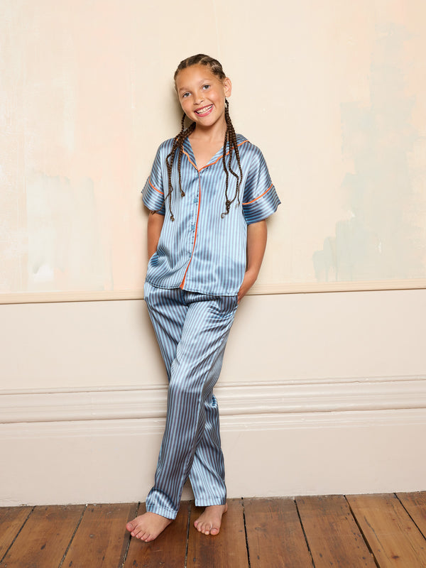 Older child wearing blue striped satin pyjamas smiling against a neutral background