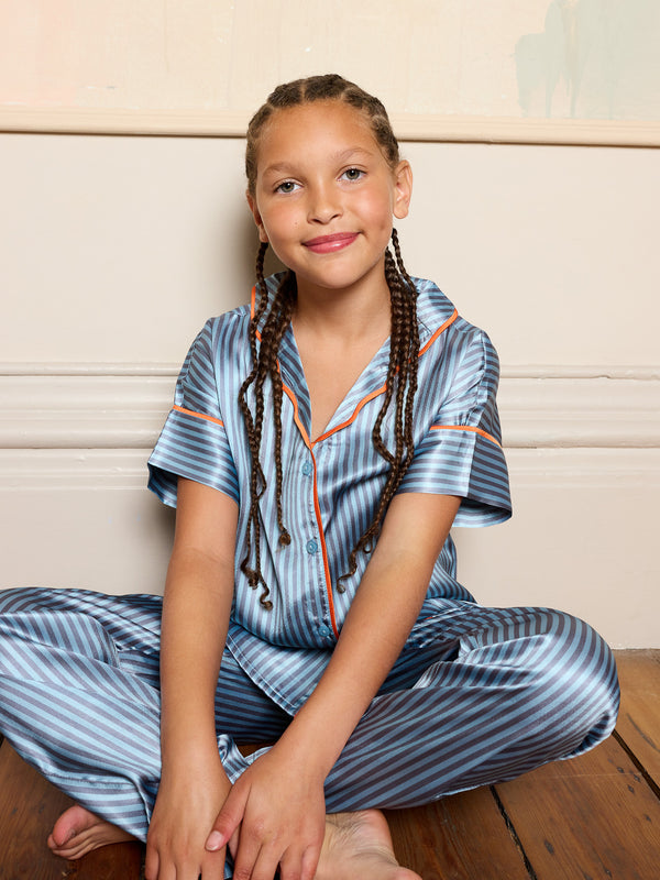 Older child wearing blue striped satin pyjamas smiling sitting on a bedroom floor