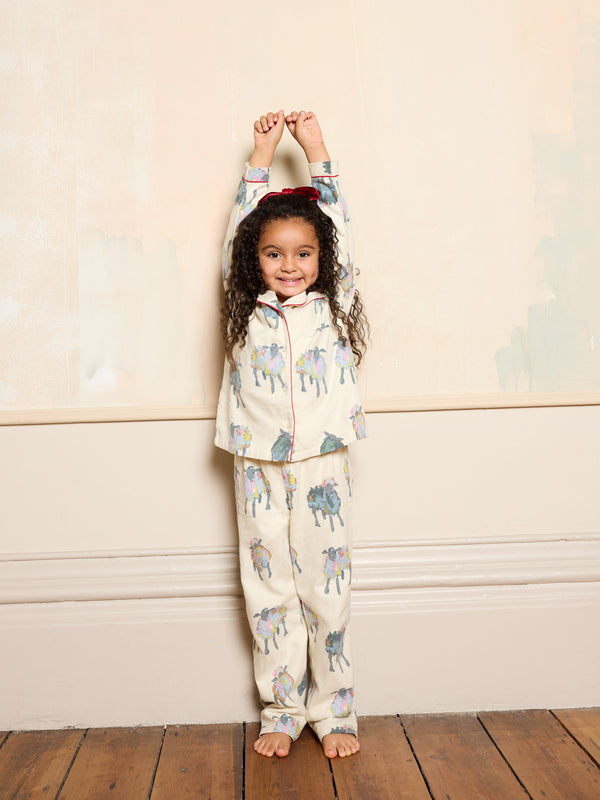 Child wearing a patterned pyjama set standing against a plain wall.