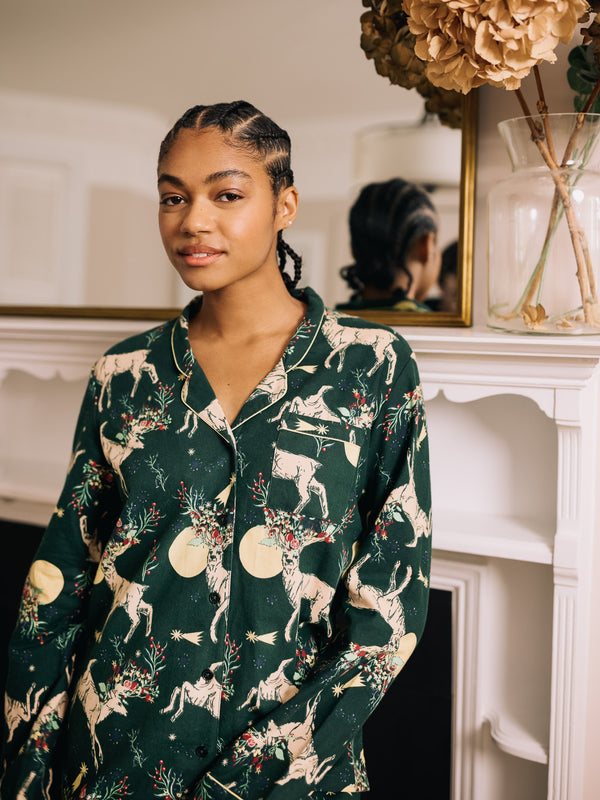 Woman wearing a dark green pyjama set with reindeer pattern in a room with decorative elements.