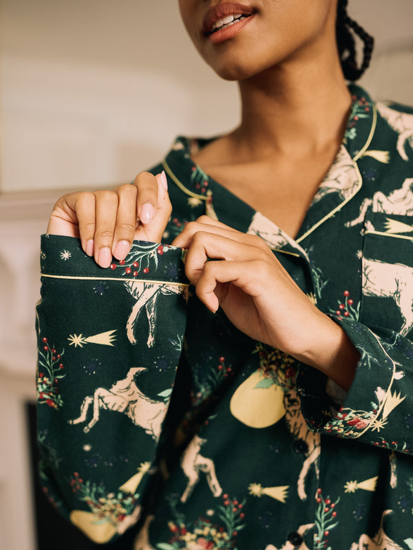 woman wearing a dark green pyjama set with reindeer pattern pointing to the soft brushed cotton fabric