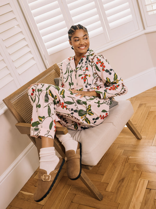 Woman sitting on a chair wearing a floral pyjamas in a room with wooden flooring and white walls.