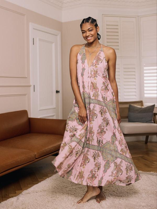 Woman in a pink floral night dress standing in a living room with a brown sofa and white walls.