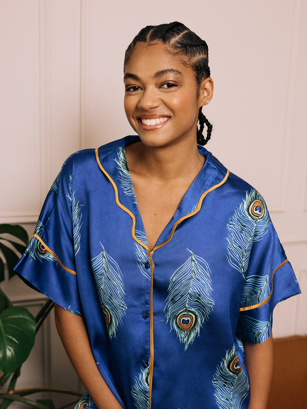 Woman wearing a blue satin pajama top with peacock feather pattern against a neutral background
