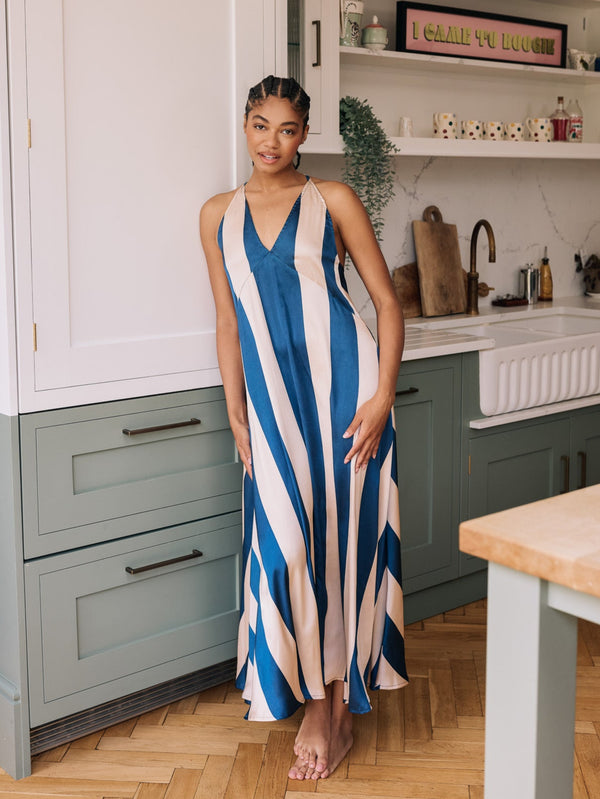 Woman in a blue and beige striped satin night dress standing in a kitchen.