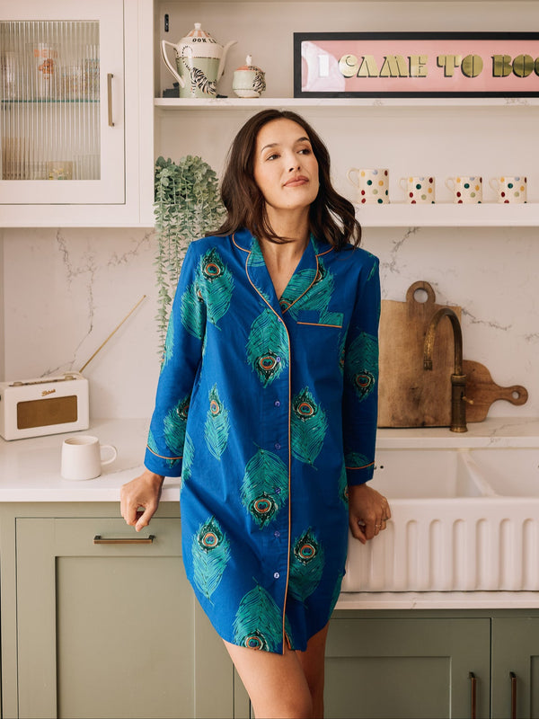 Woman wearing a blue peacock feather patterned nightshirt in a kitchen.