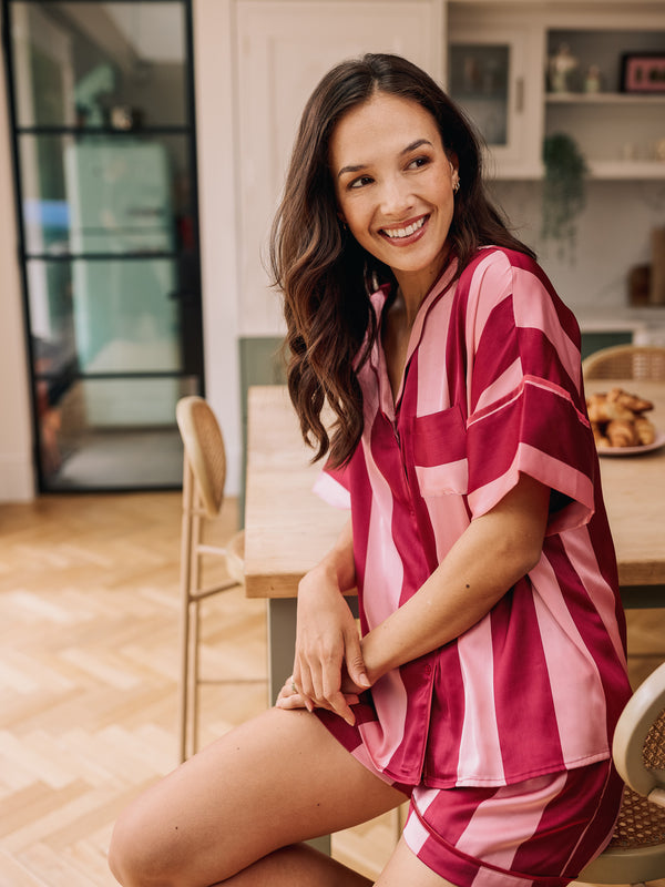 Woman wearing a pink and blush striped pyjama short set sitting in a kitchen.