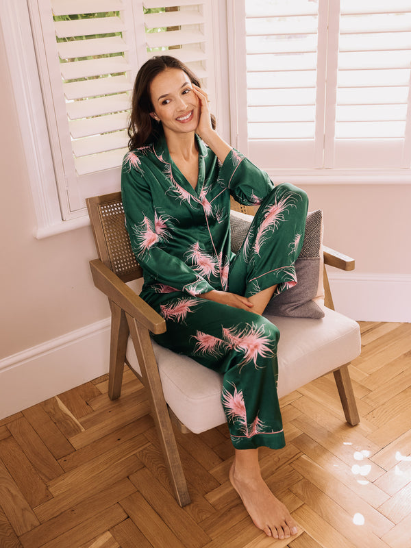 Woman wearing a green pyjama set with pink feather patterns sitting on a cosy chair