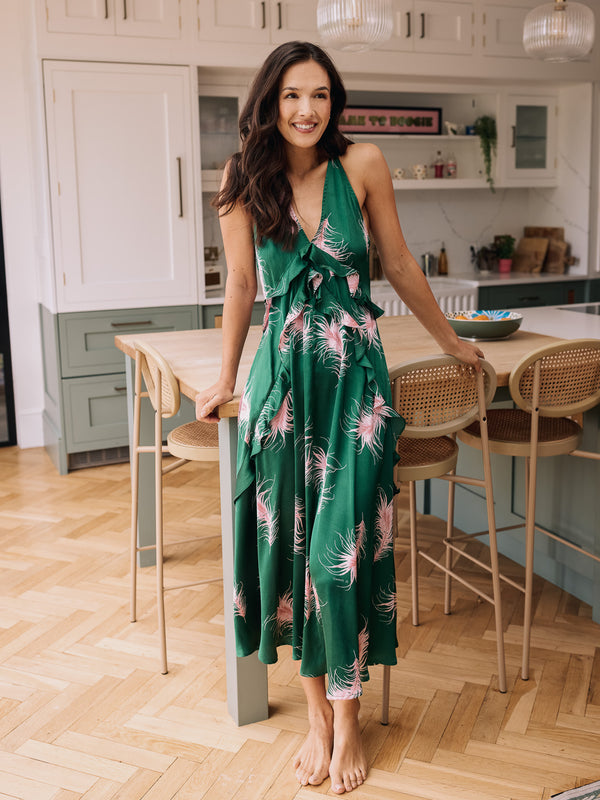 Woman in a green satin night dress with pink feather pattern standing in a kitchen.