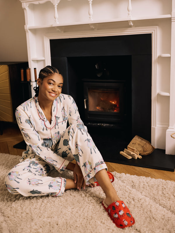 woman wearing soft brushed cotton white pyjamas with sheep pattern sitting by a cosy fireplace