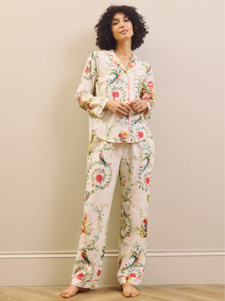 Model wears a white based floral print pyjama set against a beige wall. 