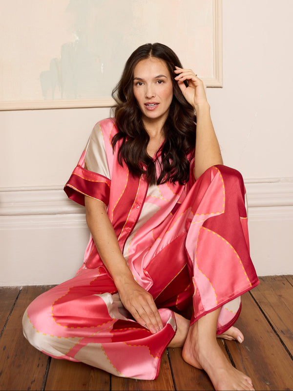 Woman wearing a pink and red satin pyjamas sitting on a wooden floor.