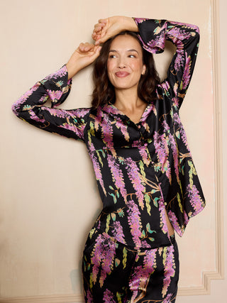woman wearing black satin pyjamas with wisteria print, featuring fluted sleeves