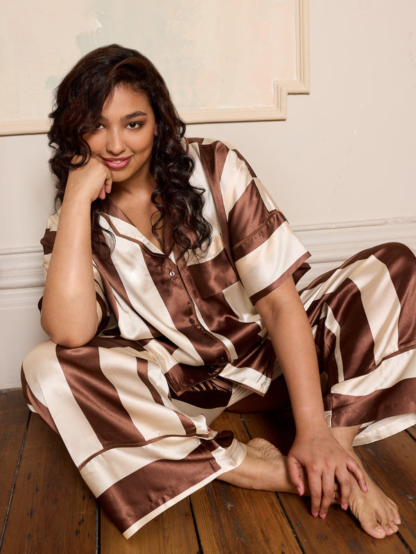 Woman wearing a brown and white striped satin pyjama set sitting on a wooden floor.