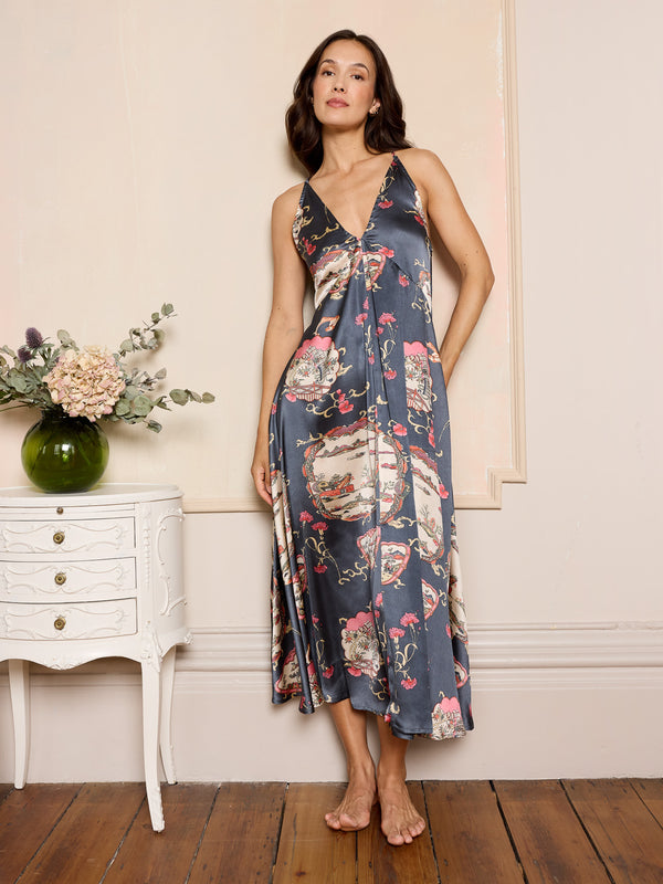 Woman wearing a grey floral night dress standing in a room with a white cabinet and flowers.