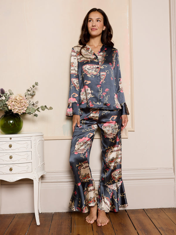 woman wearing grey satin floral pyjama set in a bedroom with a white dresser and a vase with flowers