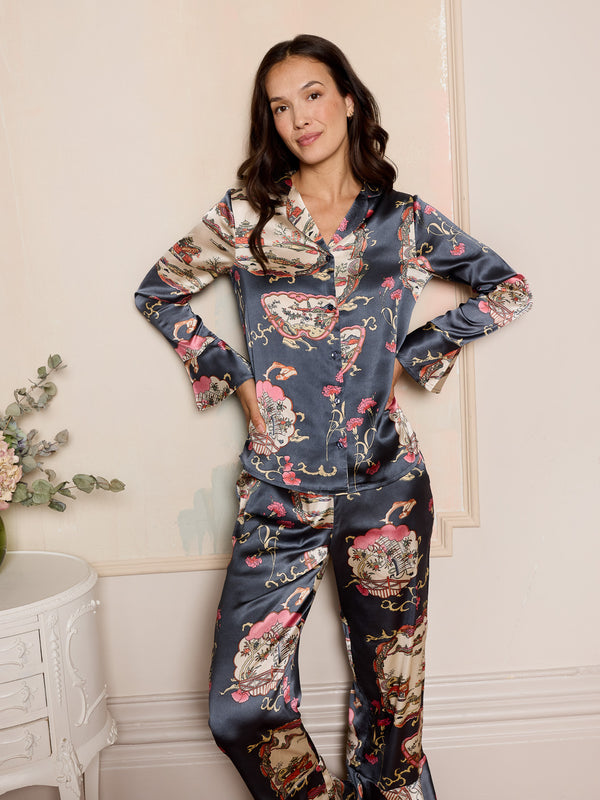 woman wearing grey satin floral pyjama set in a bedroom with a white dresser and a vase with flowers