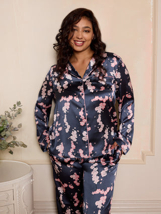 Woman wearing a satin floral pyjama set against a light-coloured wall with her hands in her trouser pockets.
