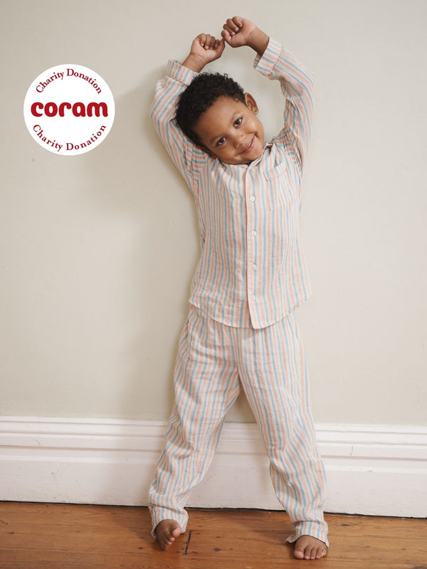 Child in striped pyjamas standing against a white wall on a wooden floor