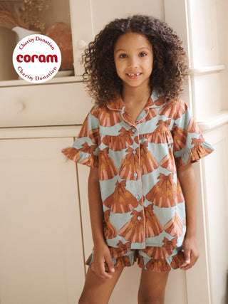 Young girl wearing a patterned pyjama set standing in a room with white cabinets.