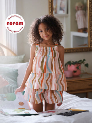 Young girl wearing a colorful striped pyjama set sat on a bed. 