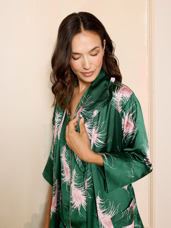 Woman wearing a green kimono robe with pink floral patterns against a beige wall.