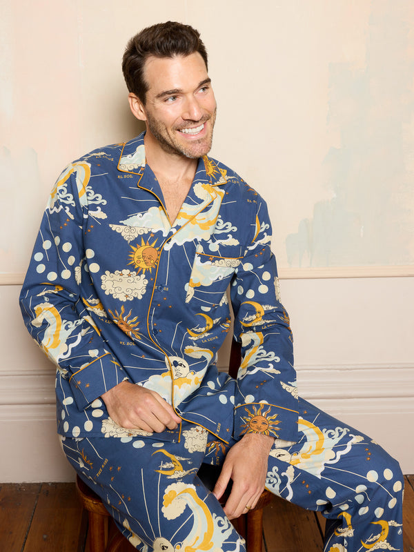 Man wearing a blue cotton pyjama set with celestial design sitting on a wooden floor.
