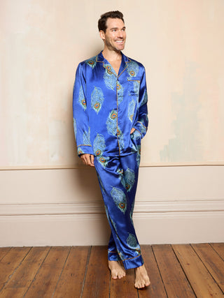 Man wearing blue satin pyjamas with peacock feather pattern against a beige wall.