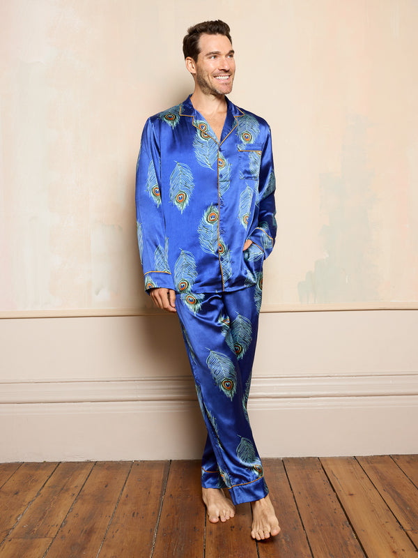 Man wearing blue satin pyjamas with peacock feather pattern against a beige wall.