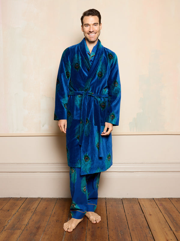 Man wearing a blue velvet robe with peacock feather pattern on a wooden floor.