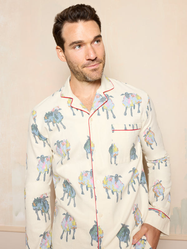 Man wearing a brushed cotton pyjama set with sheep pattern standing in a room with wooden floor and beige walls.