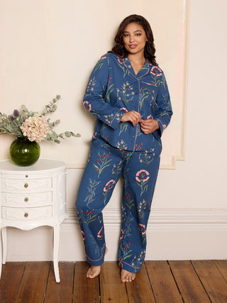 Woman wearing a blue floral pyjama set in a room with a white dresser and flowers.