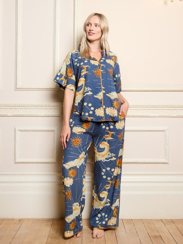 Woman wearing a blue pyjama set with celestial design against a white wall.