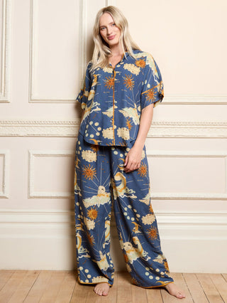 Woman wearing a blue celestial pyjama set against a white wall with a hand in her pyjama trouser pocket.