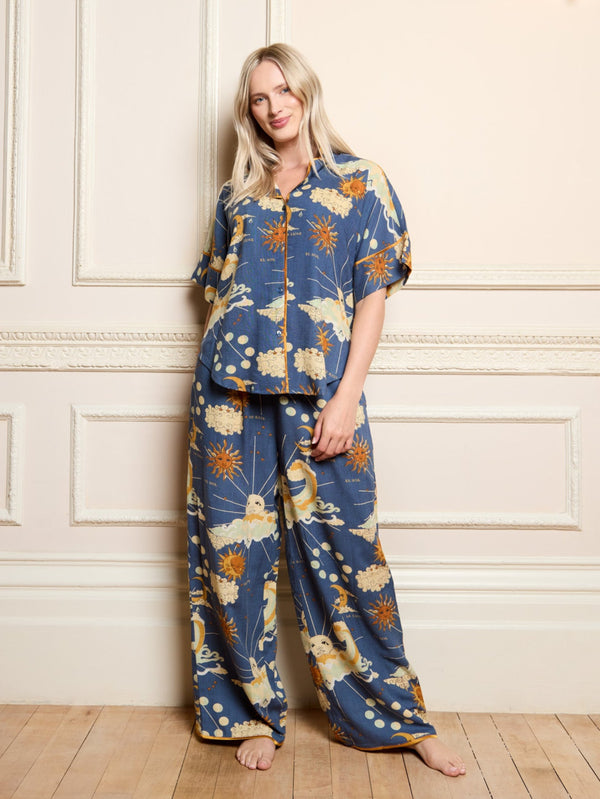 Woman wearing a blue celestial pyjama set against a white wall with a hand in her pyjama trouser pocket.