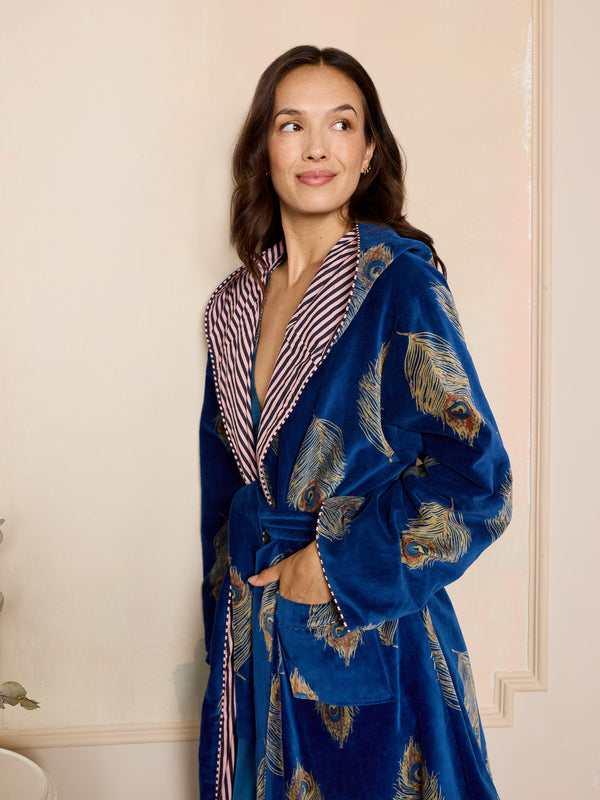 Woman wearing a blue velvet robe with peacock feather patterns in a bedroom setting