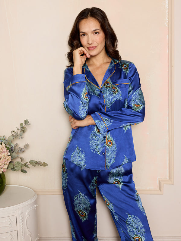 Woman wearing a blue satin pyjama set with peacock feather pattern in a room.