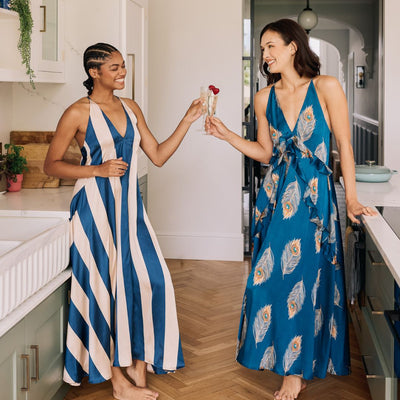 Two women in blue nighties standing in a kitchen, clinking glasses.