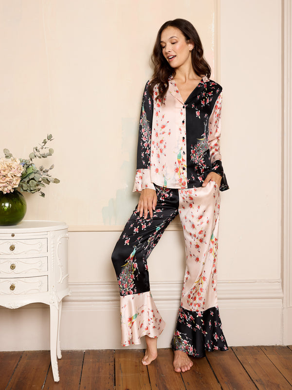 Woman wearing a pink and black floral satin pyjama set with peacock and rose pattern, fluted sleeves and bottoms