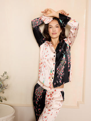 Woman wearing a pink and black floral satin pyjama set with peacock and rose pattern