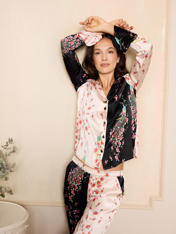 Woman wearing a pink and black floral satin pyjama set with peacock and rose pattern