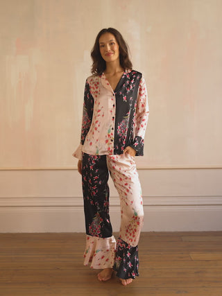 Woman wearing a pink and black floral satin pyjama set with peacock and rose pattern