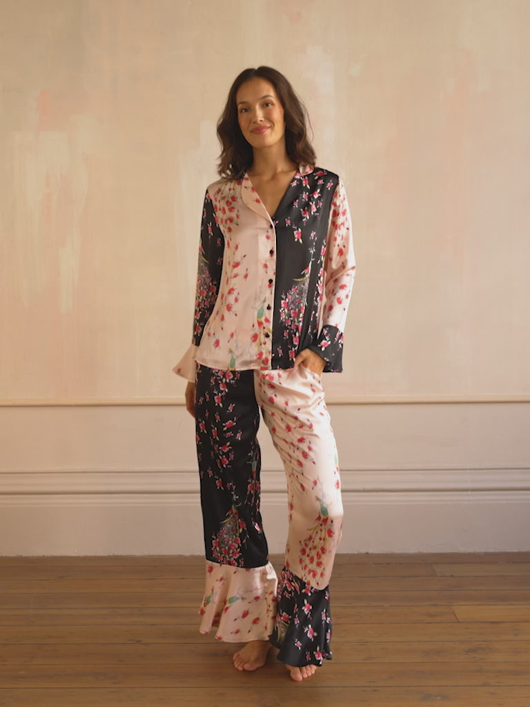 Woman wearing a pink and black floral satin pyjama set with peacock and rose pattern