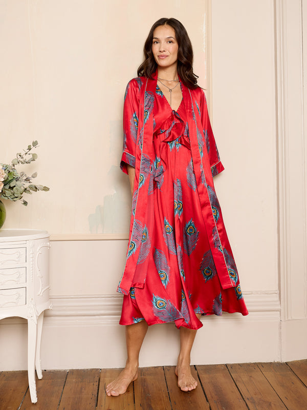 Woman wearing a red satin robe with peacock feather pattern in a room.