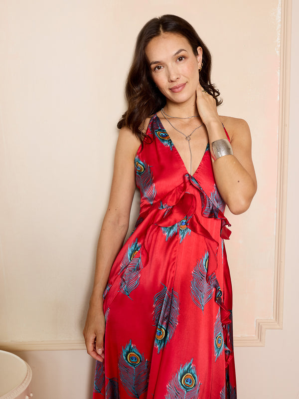 Woman wearing a red night dress with peacock feather pattern against a beige wall.