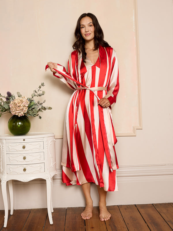 Woman wearing a red and white striped satin robe standing in a room with a white side table and flowers.